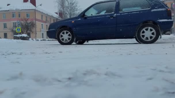 Автомобиль проходит перекрёсток рядом с пешеходным перекрестком зимой во время снегопада. Дорога покрыта снегом. Опасность проскальзывания, ДТП — стоковое видео