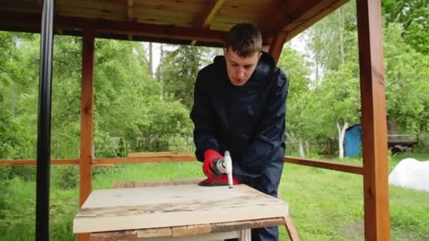 Un hombre caucásico en el campo en el verano quema un escudo de madera con un quemador de gas. Concepto de madera hecha a mano, fondo — Vídeos de Stock