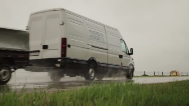 Uma carrinha com um reboque dirige em uma estrada molhada na chuva, céu cinzento. Movimento lento — Vídeo de Stock