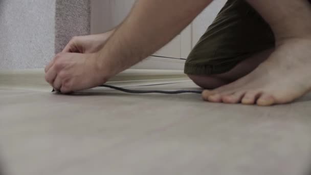Un operaio installa un nuovo battiscopa sul pavimento in un appartamento. Installazione di plinti a pavimento con viti, installazione di angoli, primo piano — Video Stock
