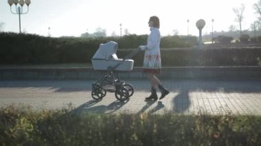 Gri paltolu ve siyah gözlüklü genç bir anne elinde bebek arabasıyla caddede yürüyor. Annelik ve aile, geçmiş, hareket