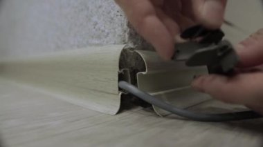 Bir işçi bir apartmanın zeminine yeni bir etek panosu yerleştiriyor. Vidalı zemin kaplamalarının kurulumu, köşelerin kurulumu, yakın plan