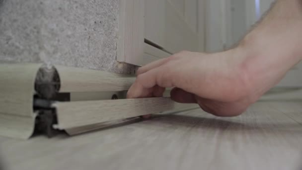 Pracownik instaluje nową listwę przypodłogową na podłodze w mieszkaniu. Montaż cokołów podłogowych ze śrubami, montaż narożników, zbliżenie — Wideo stockowe