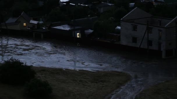 Inundación después de fuertes lluvias con truenos. El agua del río fluye por la calle del pueblo, por la noche — Vídeo de stock