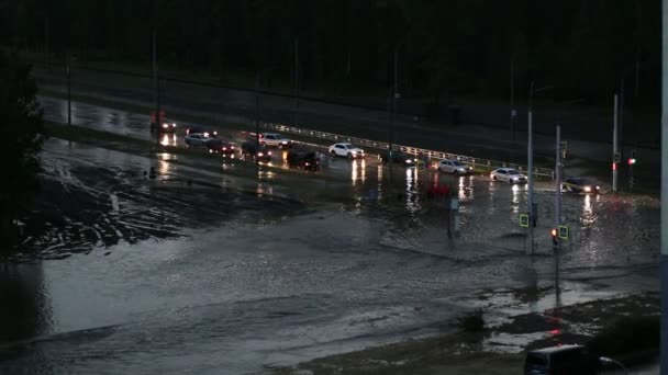 Overstroming in de stad, een stroom van water stroomt door de straat. Auto 's met koplampen op het water, het risico van autopech en waterhamer. — Stockvideo