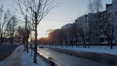 Araba, kışın dar bir cadde boyunca akşamları çok katlı binaların bulunduğu bir yerleşim bölgesinde gün batımında yol alır. Kış sonrası ilkbahar. Sıfırın üstünde. Çamur.