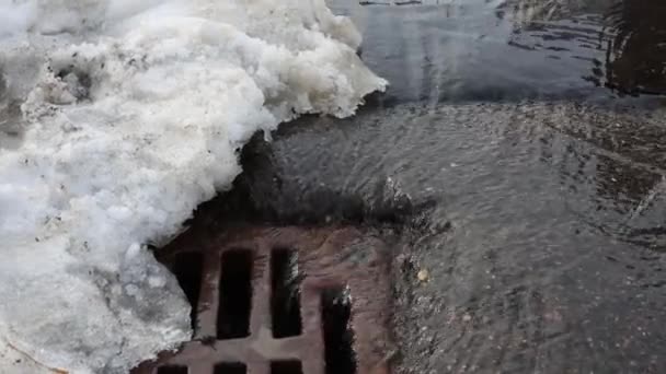 春には路上で雪が融けている。市内の水溜りや通りからの水が下水道に流れ込む。春 — ストック動画