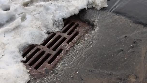 Melting snow on the street in spring. Water from puddles and streets of the city flows into the sewer. Springtime — Stock Video