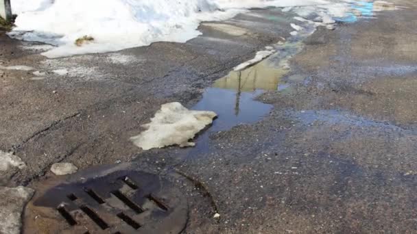 Melting snow on the street in spring. Water from puddles and streets of the city flows into the sewer. Springtime — Stock Video