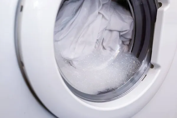 둥근 투명 한문 은자 동적 세탁기 안으로 들어가며, 그 세탁기를 통해 하얀 옷을 세탁하는 모습을 볼 수있다 — 스톡 사진