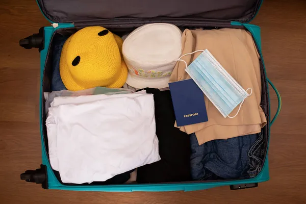 Vista superior de la maleta preparada para las vacaciones junto al mar durante una pandemia. Ropa, pasaporte con médico y máscara. — Foto de Stock