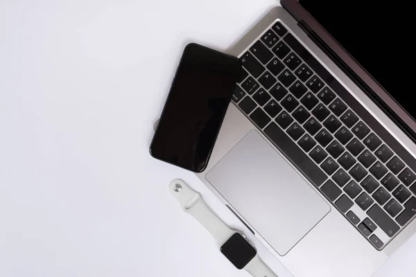 Ofis masasının en üst görüntüsü. Bilgisayarı, akıllı saati, akıllı telefonu ve kalemi olan beyaz ofis masası.