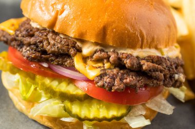 Ev yapımı Cheese Smash Burger yanında patates turşusu ve domates.