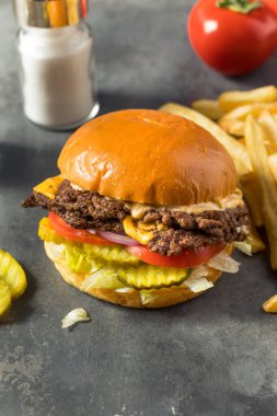 Ev yapımı Cheese Smash Burger yanında patates turşusu ve domates.