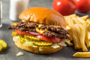 Ev yapımı Cheese Smash Burger yanında patates turşusu ve domates.