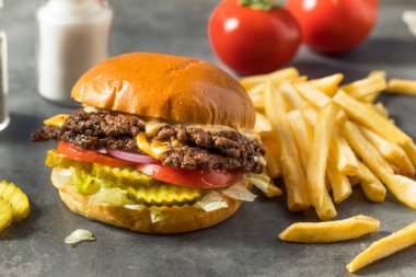 Ev yapımı Cheese Smash Burger yanında patates turşusu ve domates.