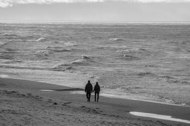 Fırtınalı bir günde Palanga sahillerinde yürüyen insanlar.