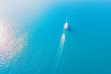 Beyaz Lüks Yat, temiz mavi deniz yüzeyinde seyrediyor. Gökyüzünden açık turkuaz sihirli denizdeki teknenin üzerinden hava manzarası.
