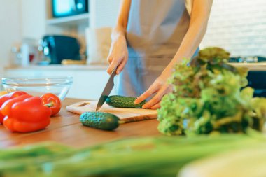 Genç bir kadın modern, rahat mutfağın içinde taze sebze salatası kesiyor, sağlıklı bir yemek hazırlıyor.