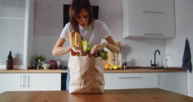 Kadın mutfak tezgahındaki alışveriş poşetinden sebze boşaltıyor vejetaryen yemekleri ve yemek pişirme konsepti.