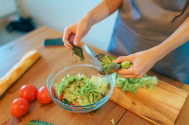 Genç bir kadın modern, rahat mutfağın içinde taze sebze salatası kesiyor, sağlıklı bir yemek hazırlıyor.