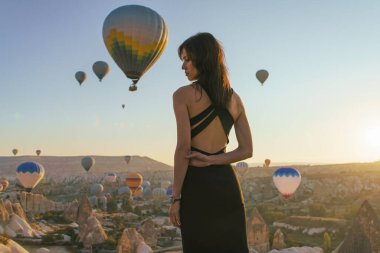 Kapadokya, Goreme, Türkiye 'deki vadide güneşin doğuşunu ve sıcak hava balonlarının yükselişini izleyen kadın