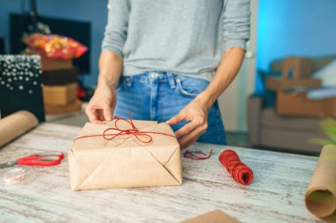 Bayram hediyelerini paketleyen kadın, şık hediyeleri evdeki masada el işi kağıtlarıyla süsleyen kadın.