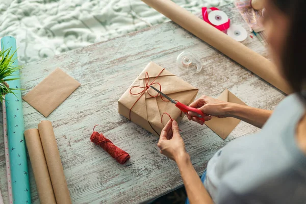 Evdeki masada hediye paketi yapan genç bir kadının genel görünümü.