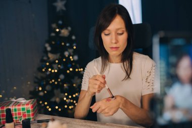 Modayı takip eden güzellik blogcusu Noel arifesinde Noel ağacı arka planında güzellik kozmetiklerini sunar. Blogger konsepti