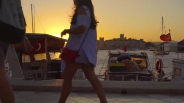 Gün batımında Bodrum limanında rıhtımlı tekne ve yatlarla yürüyen insanlar, Türkiye