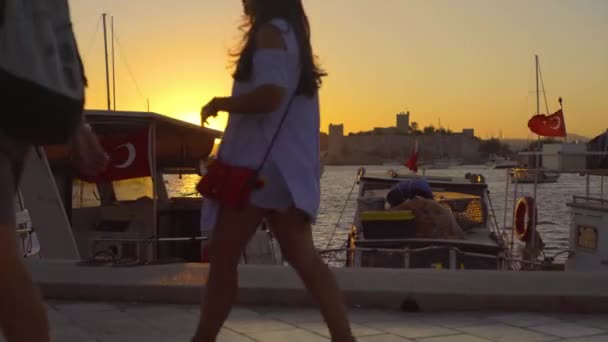 Gün batımında Bodrum limanında rıhtımlı tekne ve yatlarla yürüyen insanlar, Türkiye — Stok video