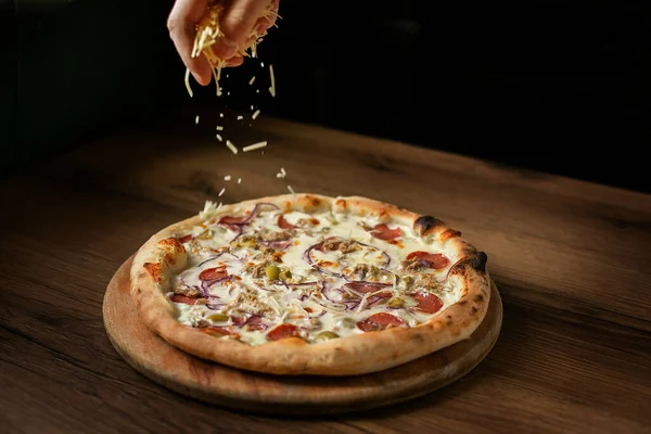 Şef pizzaya peynir serpiyor. Koyu bir arka planda, boş alan.