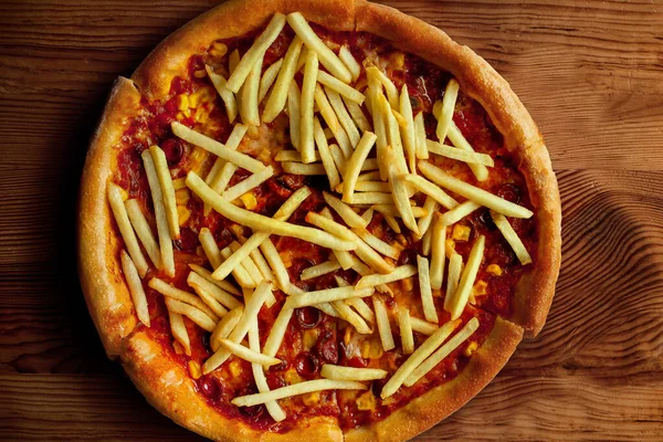 Tomato pizza with French fries on it. wooden table. top view