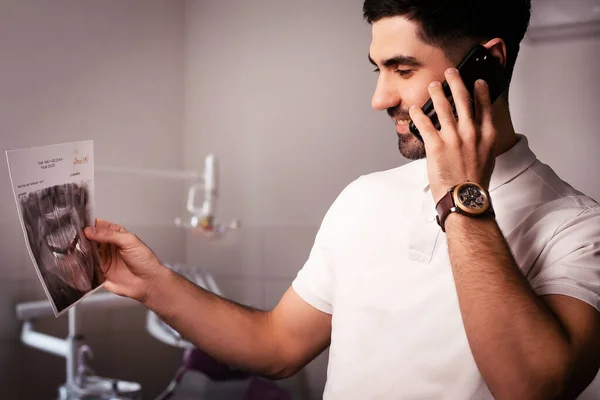 Dentist looking an X-ray of jaw with an implanted tooth. talking on the phone