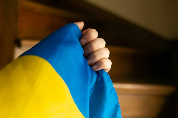 hand with small ukrainian flag wooden stairs background