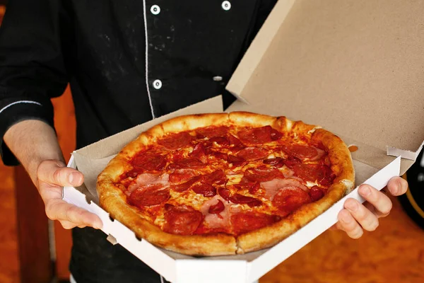 pizza chef wearing black apron holding freshly baked pizza in open box