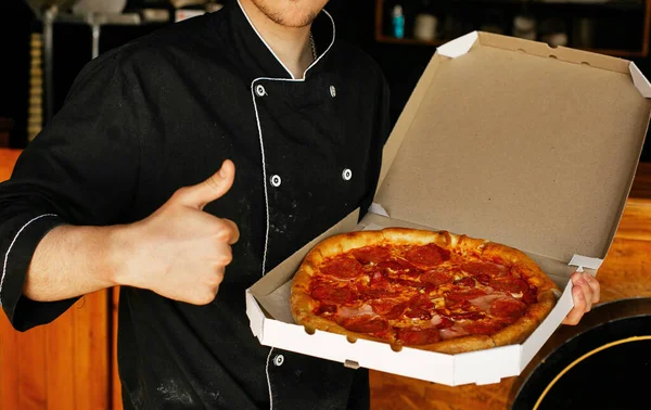pizza chef wearing black apron holding freshly baked pizza in open box at pizza shop pizzeria