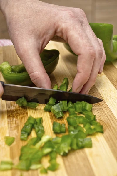 Vrouw hand snijden een groene paprika in keuken. — Stockfoto