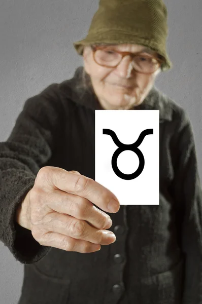 Elderly woman holding card with printed horoscope Taurus sign. — Stock Photo, Image