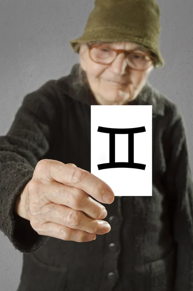 Elderly woman holding card with printed horoscope Gemini sign. — Stock Photo, Image