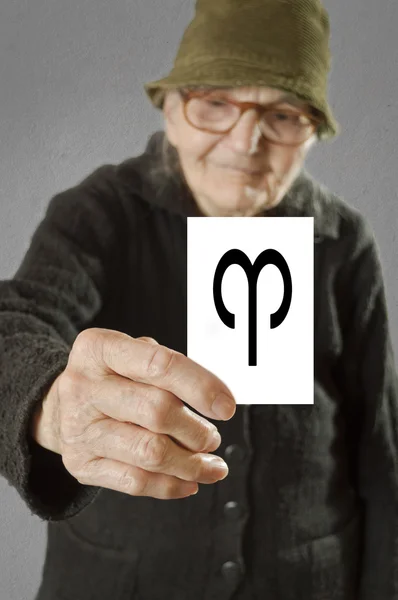 Elderly woman holding card with printed horoscope Aries sign. — Stock Photo, Image