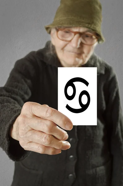 Oudere vrouw met kaart met gedrukte Horoscoop kanker teken. — Stockfoto