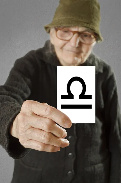 Elderly woman holding card with printed horoscope Libra sign. — Stock Photo, Image