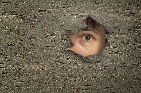 Eye looking through a hole in wall. — Stock Photo, Image