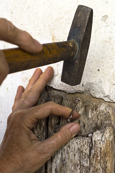 Hand holds a nail while hitting it with a hammer — Stock Photo, Image