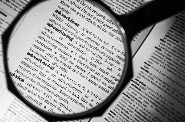 Magnifying glass on the advertising in dictionary — Stock Photo, Image