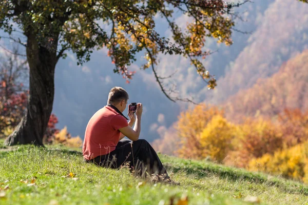 Man taking photos under autumn tree — Stock Photo, Image