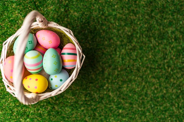 カラフルな黄色、ピンク、織りバスケットや緑の芝生の中で青イースターの卵とイースターの背景。コピースペース付きのトップビュー。イースターの祝日のバナーとヘッダー. — ストック写真