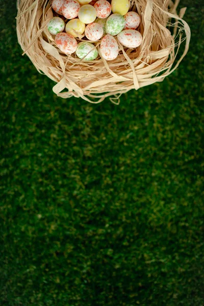 Húsvéti háttér színes sárga, rózsaszín, kék húsvéti tojás szőtt kosárban és zöld fű. Felülnézet fénymásoló felülettel. Húsvéti ünnepek zászló és fejléc. — Stock Fotó