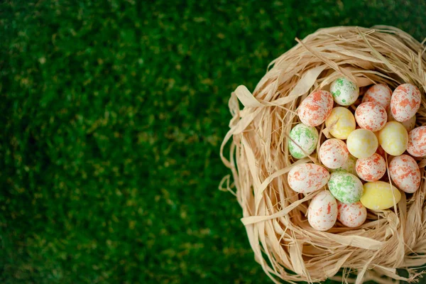 Húsvéti háttér színes sárga, rózsaszín, kék húsvéti tojás szőtt kosárban és zöld fű. Felülnézet fénymásoló felülettel. Húsvéti ünnepek zászló és fejléc. — Stock Fotó